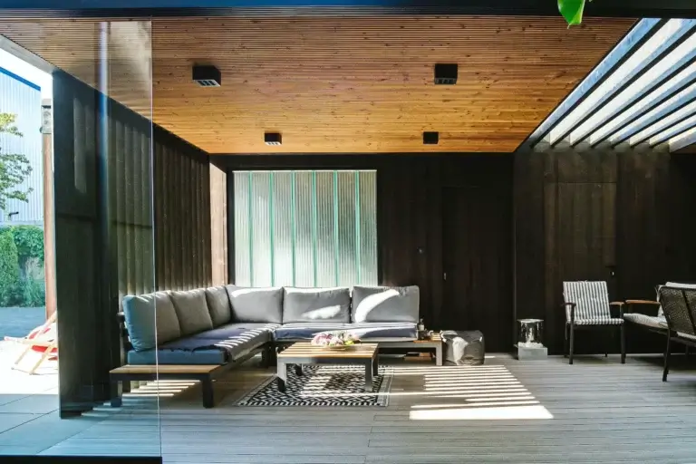 Salon ogrodowy urządzony w minimalistycznym stylu w altanie drewnianej. Czarne ściany i sufit z lameli.