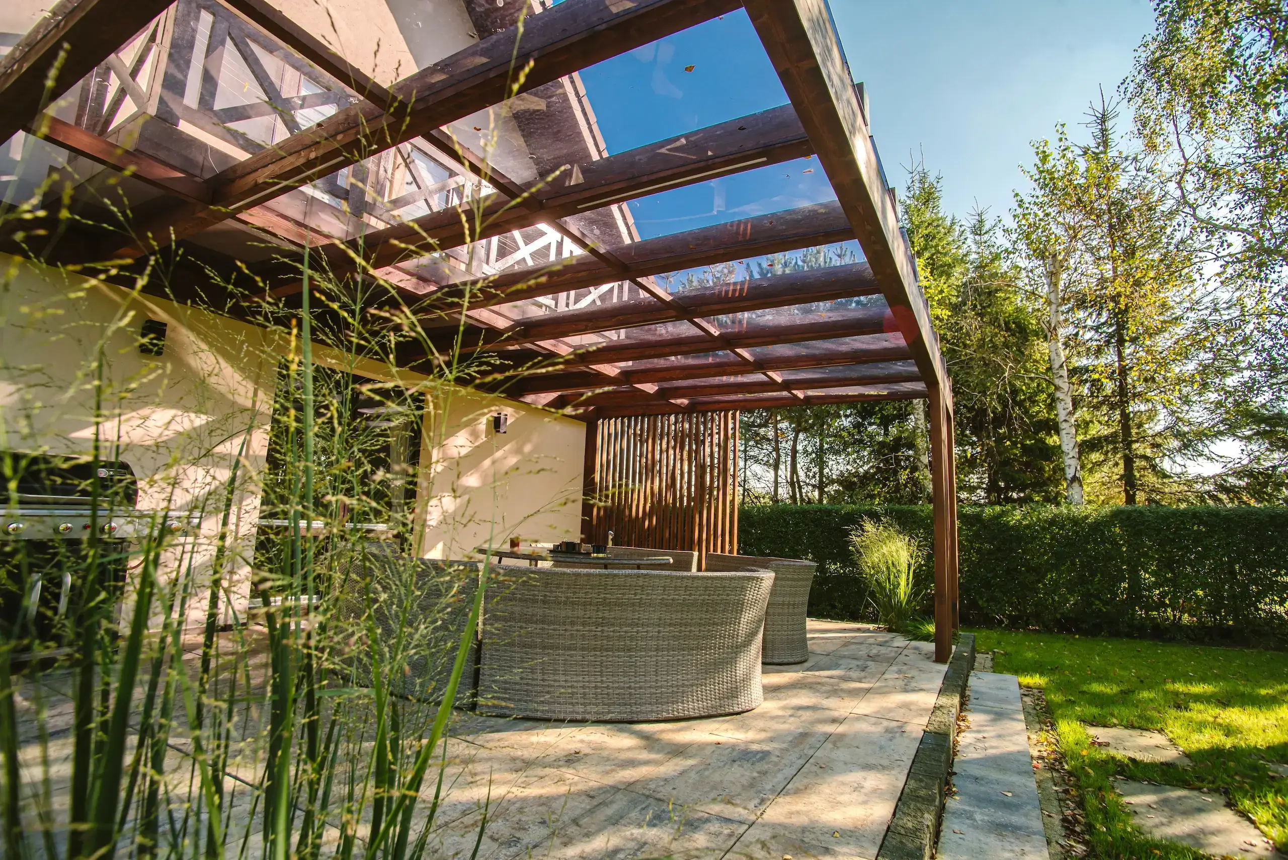 Zadaszenie tarasu ze szkła z poprzecznymi belkami z drewna.