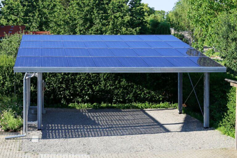 Na zdjęciu widoczny jest carport zintegrowany z instalacją fotowoltaiczną. Zadaszenie pełni funkcję parkingu dla samochodów oraz wykorzystuje energię słoneczną do wytwarzania prądu.