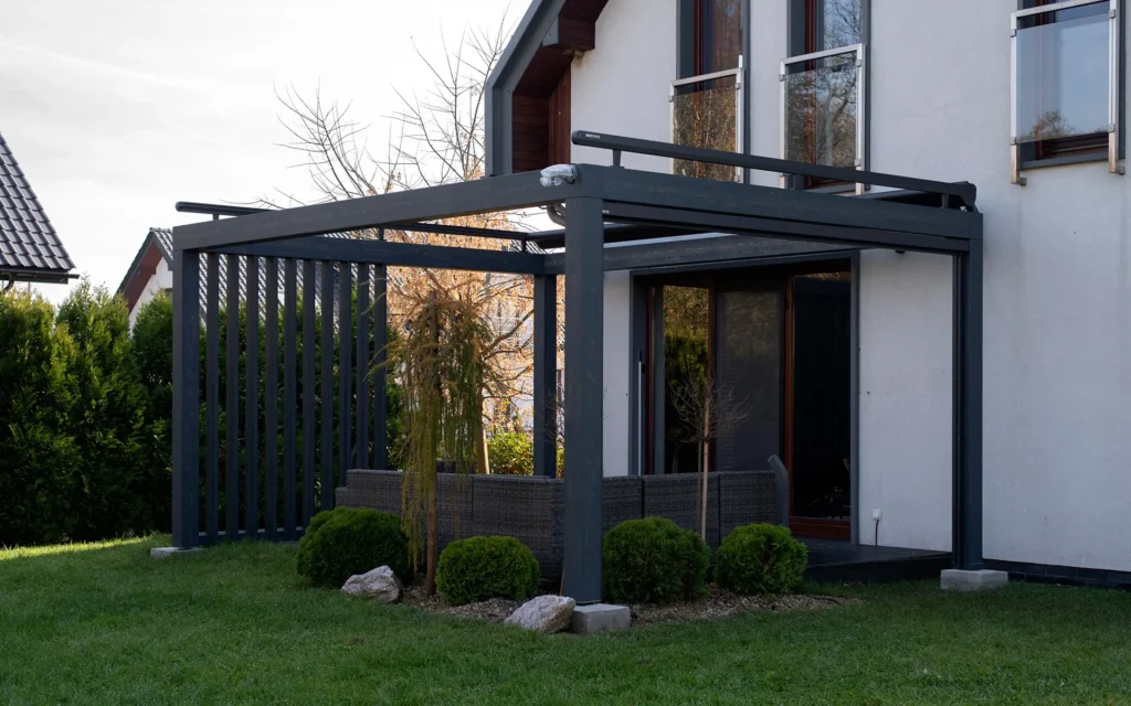 Nowoczesna pergola przydomowa z grafitowymi lamelami i sofą ogrodową — realizacja Pinegard.